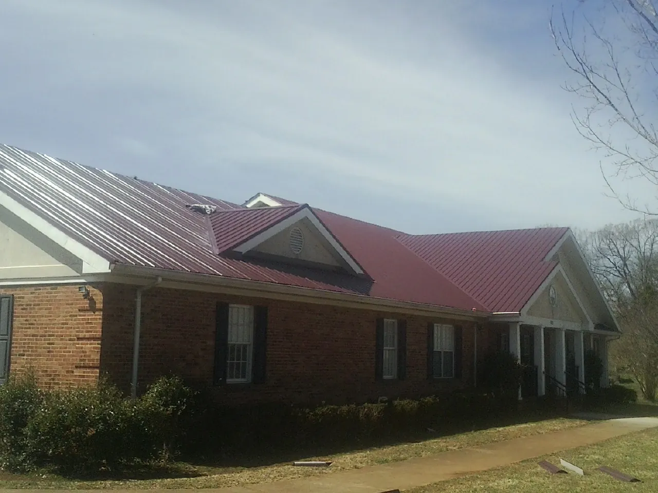 Red metal roof with gabled entries on a long brick building, from a Hail Damage Roof Repair job in Mattapan