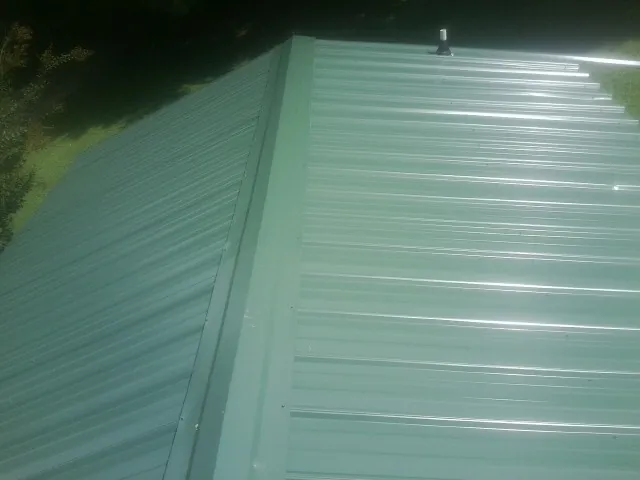 New green metal panels meeting at the ridge of a roof — Flat Roof Repair work by our crew in Mattapan