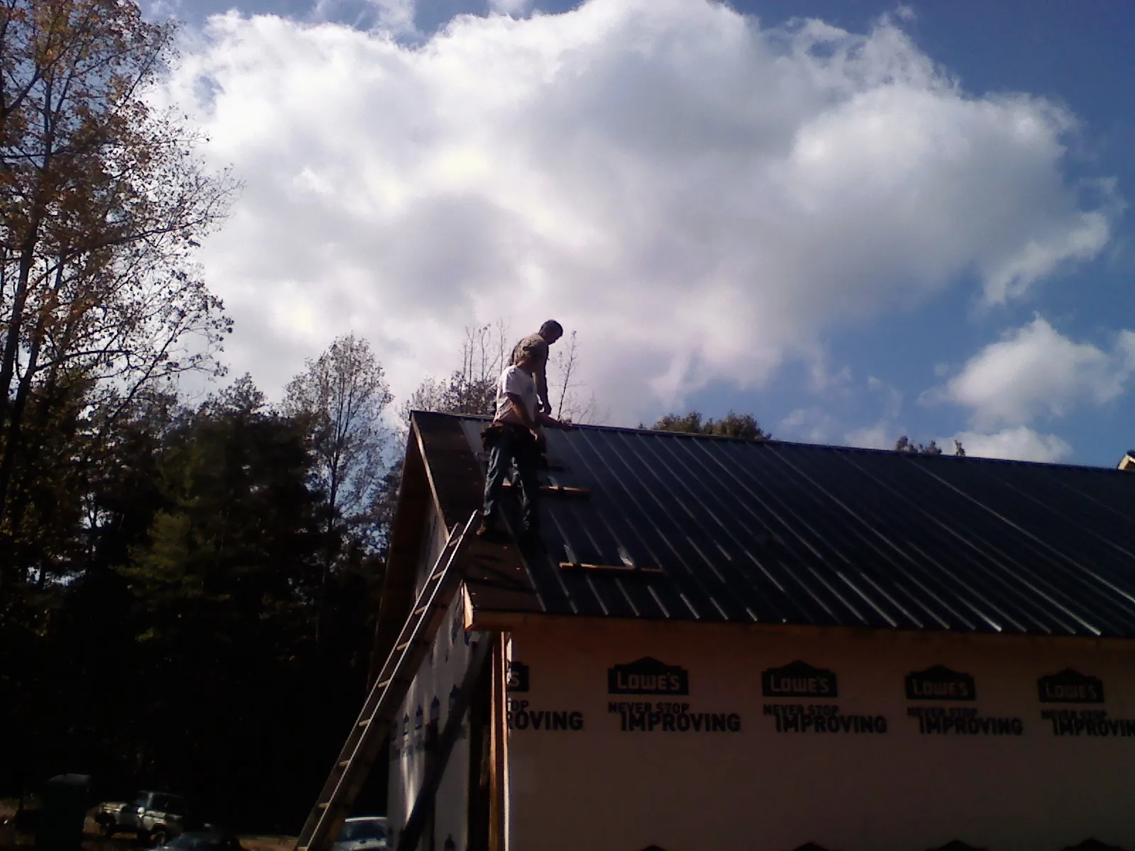 Roofer fastening dark metal panels high against a cloudy sky, from a Roof Inspection job in Mattapan