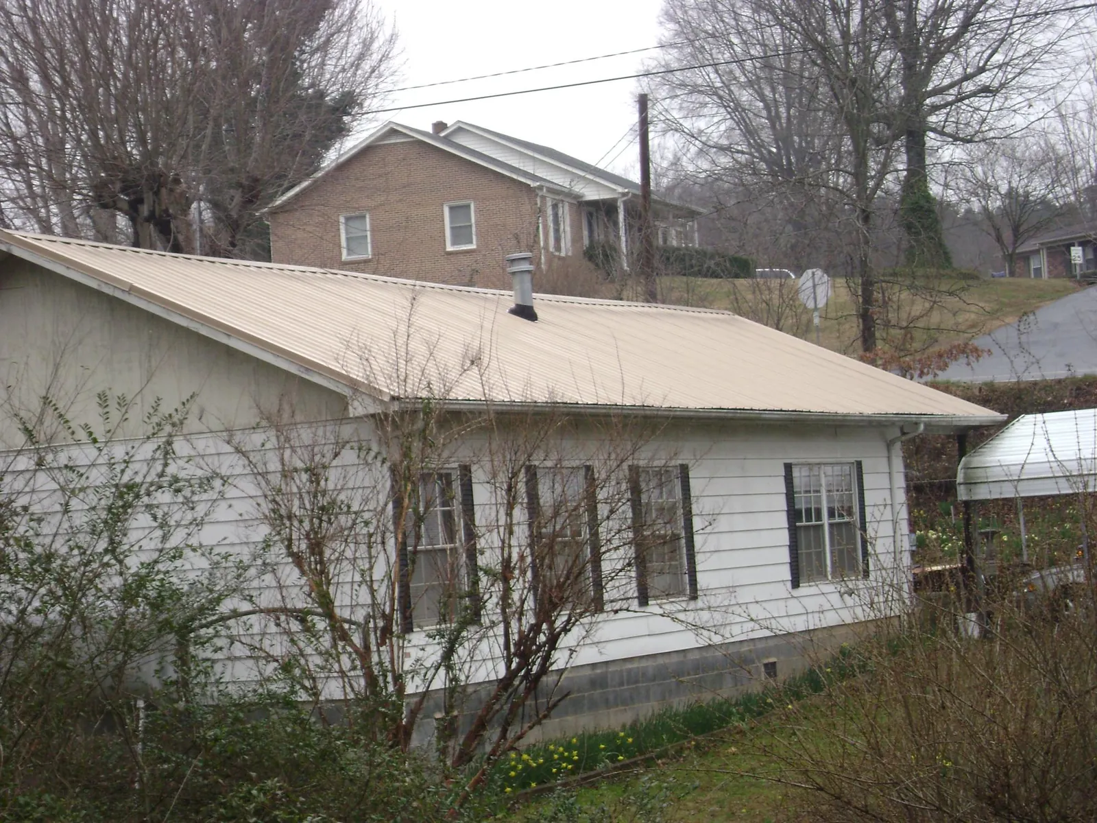 Tan metal roof on a white sided house set into a hillside — Commercial Roofing by Roofing Brothers in Mattapan