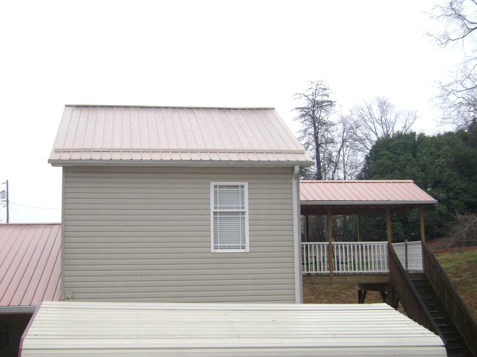 Tan metal roofs on a two story addition and attached porch, from a Roof Replacement job in Mattapan